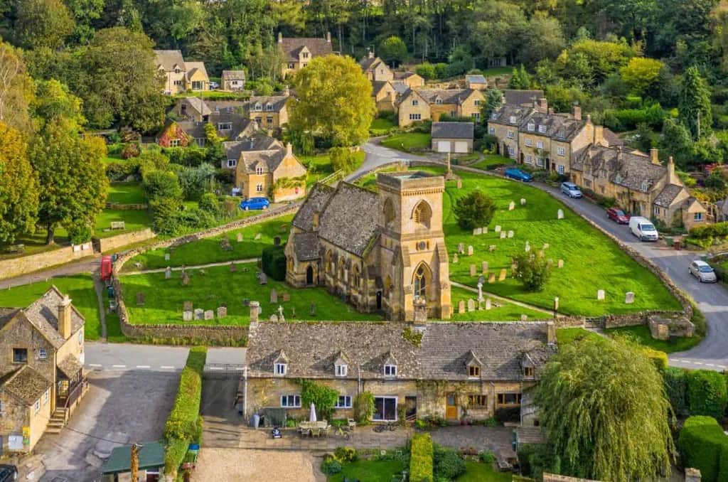 Aerial view of a classic Cotswold village with a stone church, honey-coloured cottages, and green churchyard
